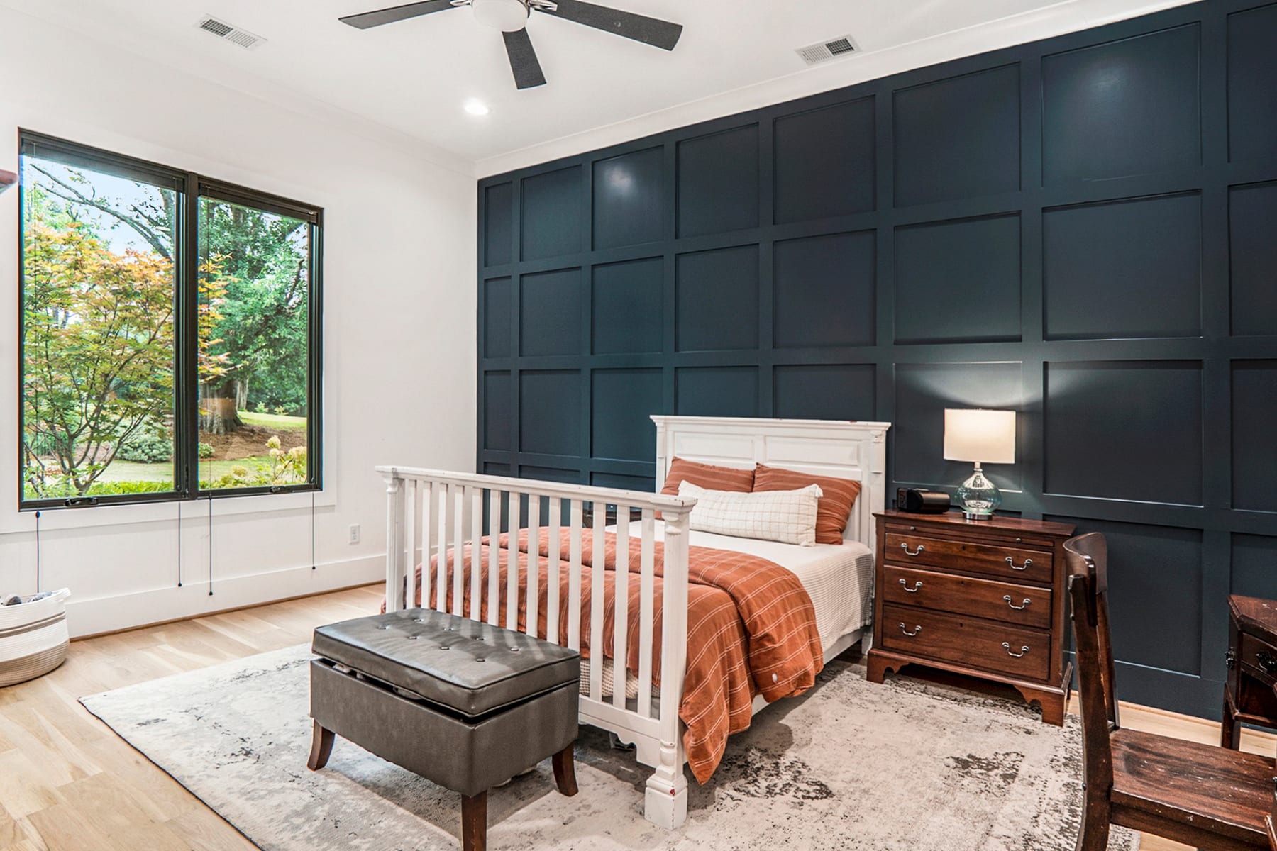 Guest bedroom with deep blue wall paneling, warm bedding, and tall corner windows