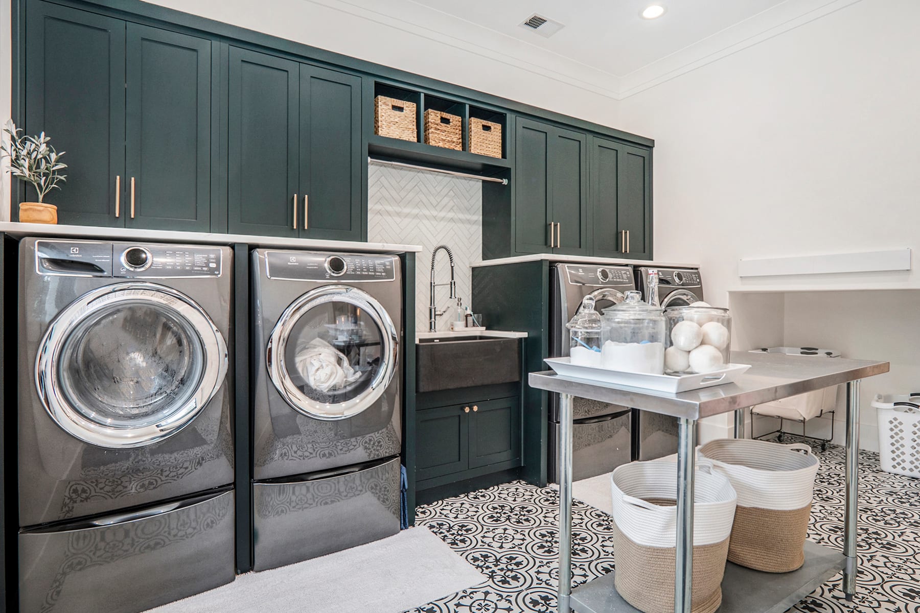 Laundry room with deep green cabinetry, patterned tile floor, and a herringbone backsplash